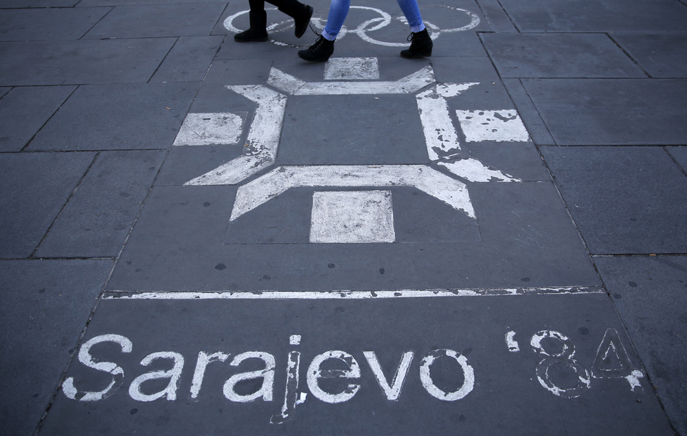 People walk past the logo of the Winter Olympics in Sarajevo, painted on the streets in central Sarajevo
